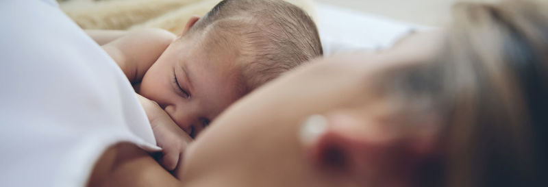 High angle view of mother breastfeeding daughter on bed at home