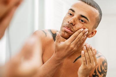 Shirtless young man applying facial mask reflecting on mirror in bathroom at home