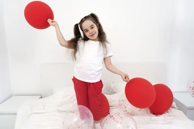 Portrait of young woman with balloons against wall