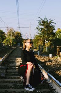 Young woman looking away while sitting on railroad track