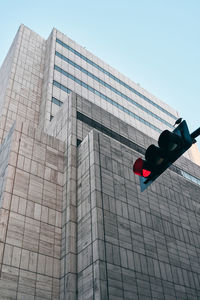 From below of black traffic light with red color and modern building with creative architecture under blue sky on background