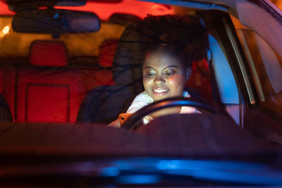 Woman typing in smartphone driving car. black girl read sms on phone sitting on driver seat at night