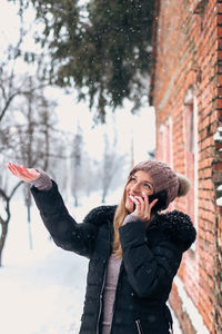 Portrait of young woman using phone while standing in winter