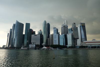 Skyscrapers by river against sky in city