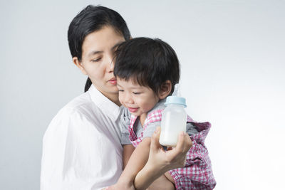 Mother holding milk bottle with daughter against white background