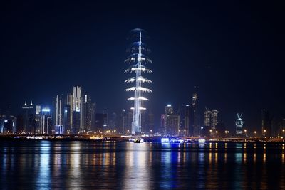 Illuminated buildings by river against sky at night