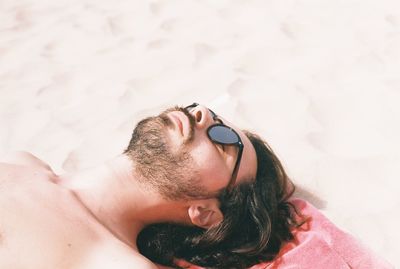 High angle view of shirtless young man lying on sand at beach during sunny day