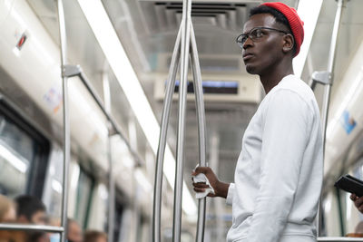 Portrait of thoughtful black student man in red hat holding handrail with napkin in subway train.