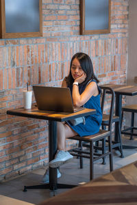 Young woman using mobile phone while sitting on table