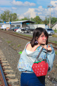 Portrait of young woman wearing sunglasses holding purse standing on railroad track