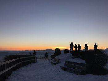 People on snow covered observation point against sky during sunset