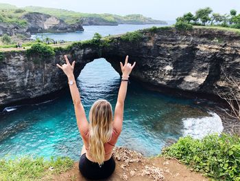 Rear view of woman with arms raised on rock