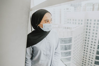 Portrait of young woman wearing facemask standing against wall 