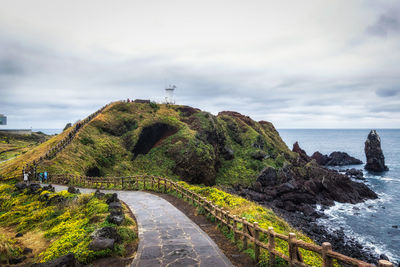 Road by sea against cloudy sky