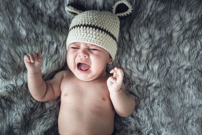 Cute baby girl in knit hat crying while lying on bed