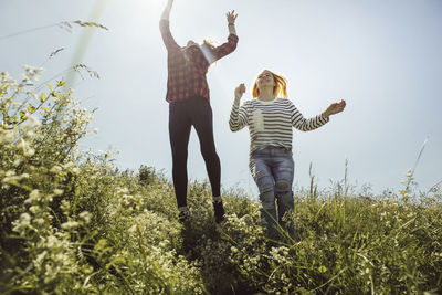 Playful female friends jumping on grassy field against clear sky during summer