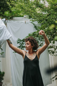 Young woman standing by plants against trees