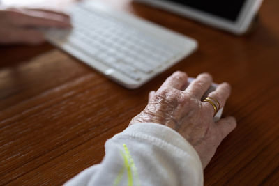 Crop anonymous patient with keyboard against tablet with doctor on screen during video call in house