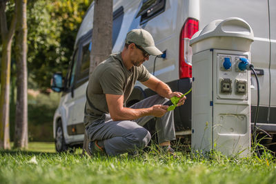 Man holding electric plug while charging car outdoors