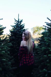 Rear view of young woman with hand in hair standing against pine trees