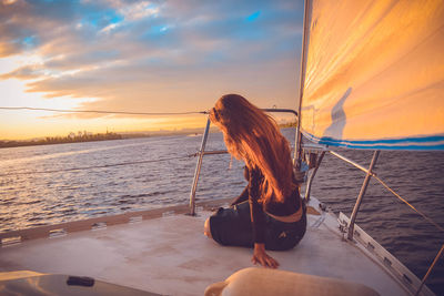 Woman sitting on shore against sky during sunset