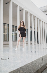 Portrait of young woman standing against building