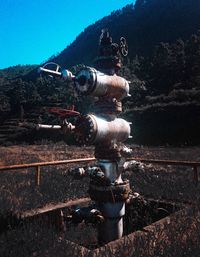 Close-up of rusty machine part on field against sky