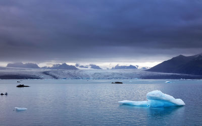 Scenic view of iceberg in lagoon against sky