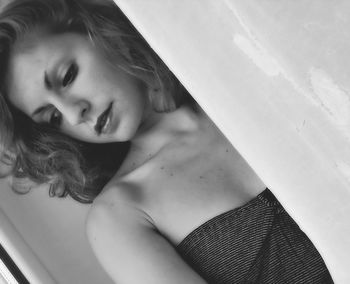 Close-up of beautiful young woman looking down while standing by curtain