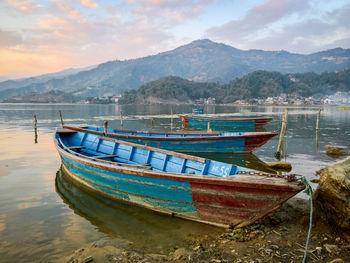 Boats moored on lake against mountains during sunset