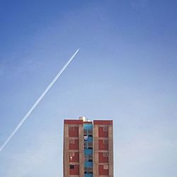 Low angle view of vapor trail and residential building against clear blue sky