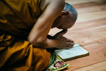 CLOSE-UP OF MAN HOLDING BOOK WHILE SITTING ON WOOD