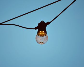 Low angle view of light bulb hanging on cable against sky