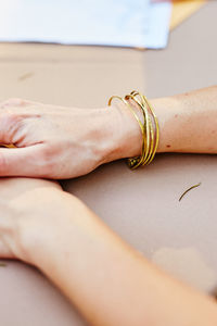 Cropped hands of woman wearing golden bangles on table