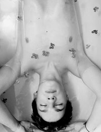 Directly above view of shirtless man sleeping with flowers in bathtub