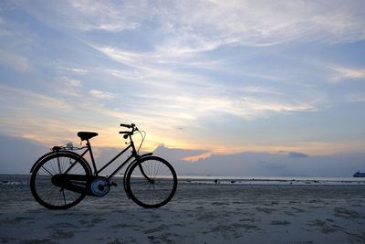 Bicycle on beach against sky during sunset
