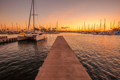 Sailboats moored on sea against sky during sunset