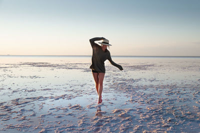 Attractive young caucasian woman in a straw hat and long jacket walks balancing on a shallow salt 