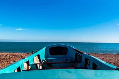 Cropped image of turquoise boat moored at beach against blue sky
