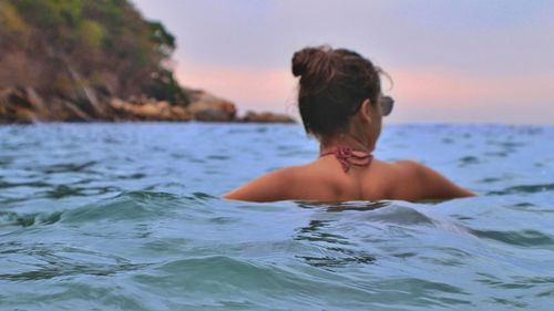 Rear view of shirtless woman in sea against sky