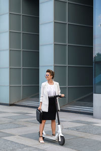 Full length of businesswoman standing by push scooter on street