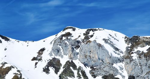 Low angle view of snowcapped mountains against blue sky