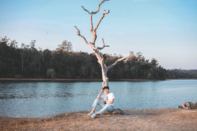 Man sitting by lake against sky