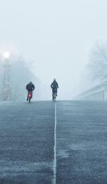 Rear view of people in foggy weather against sky during winter