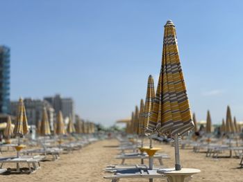 Lounge chairs and tables at beach against clear sky