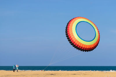 Low angle view of large colorful kite flying over beach against clear blue sky