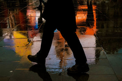 Low section of man standing on wet footpath