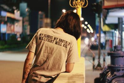 Rear view of woman with text on street in city at night
