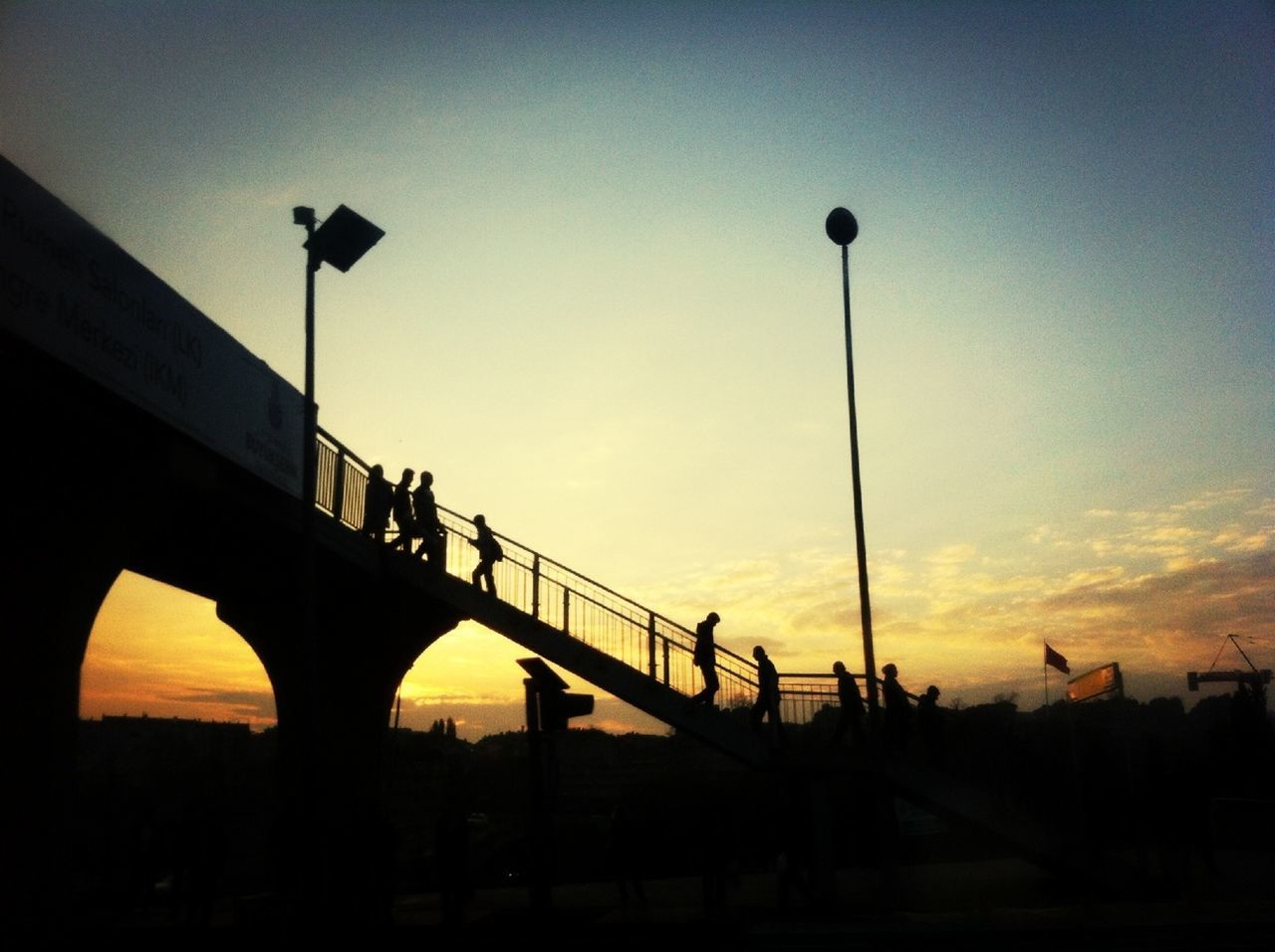 silhouette, sunset, built structure, architecture, street light, connection, bridge - man made structure, sky, low angle view, transportation, dusk, bridge, engineering, orange color, railing, clear sky, lighting equipment, copy space, outdoors, incidental people