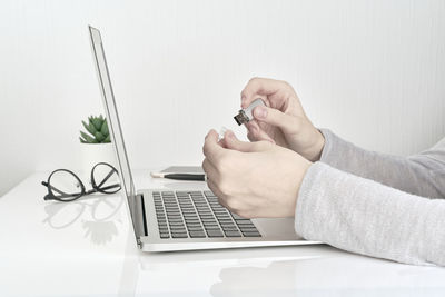 Cropped hands holding usb stick by laptop